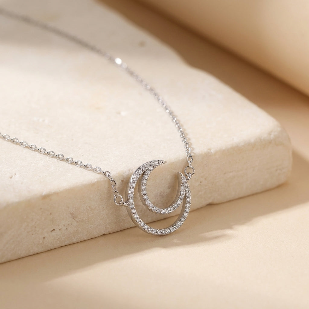 Sterling silver crescent moon necklace displayed on neutral stone background